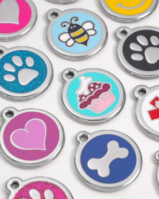 Close-up of genuine Red Dingo enamel ID tags in bright colours, including bee, cupcake, smiley, heart, bone and glitter paw print designs