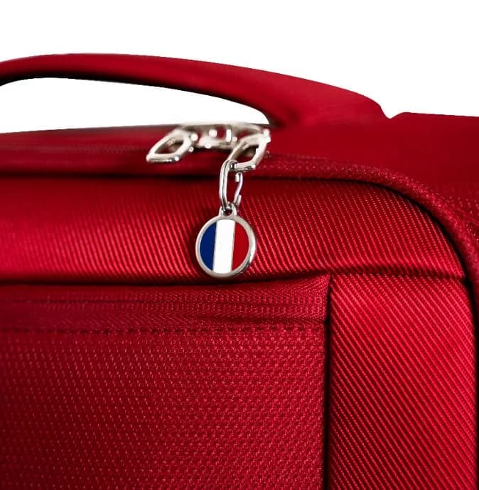 A red suitcase with a round enamel French flag ID tag clipped to the zip pull