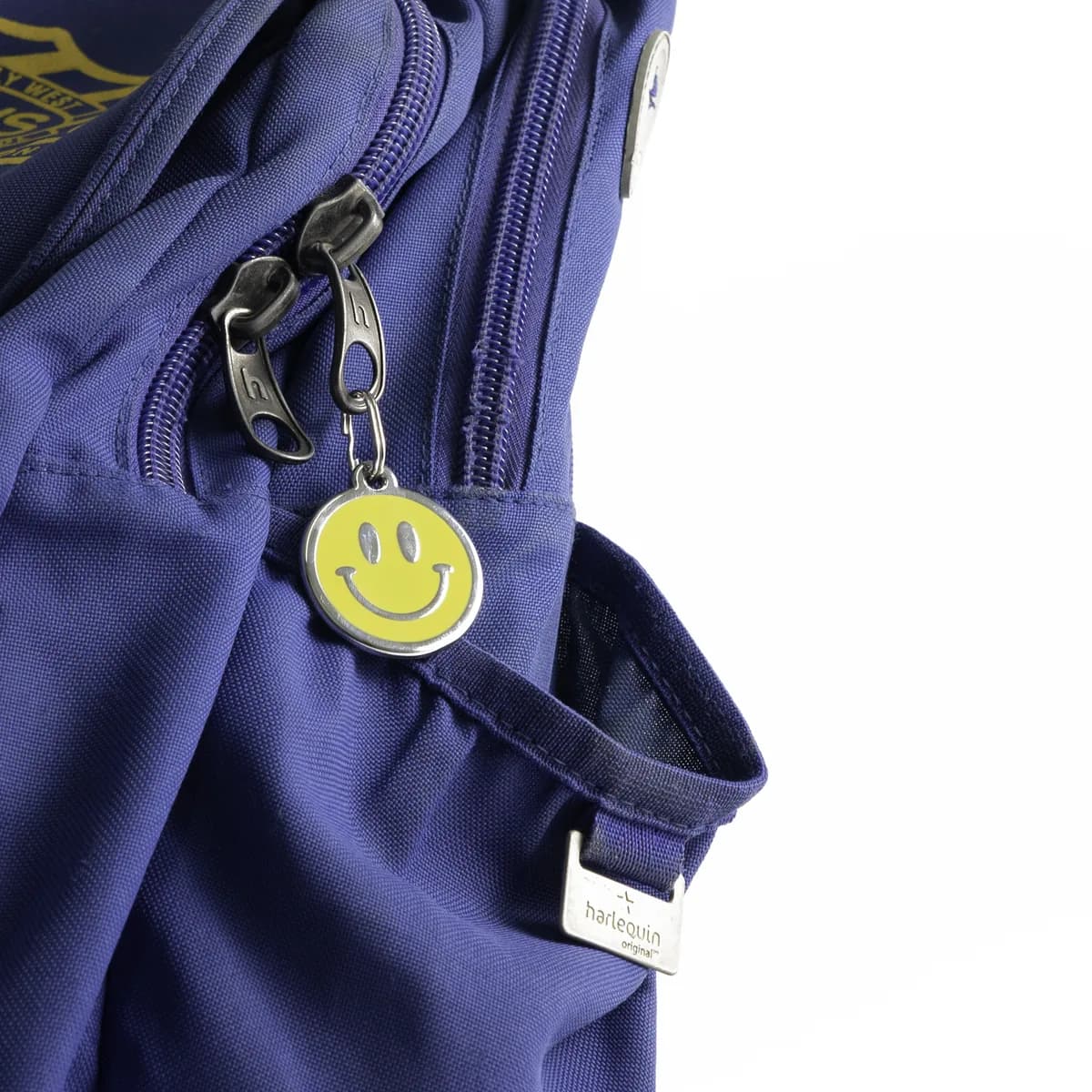 A navy school backpack with a round enamel yellow smiley face ID tag clipped to the zip